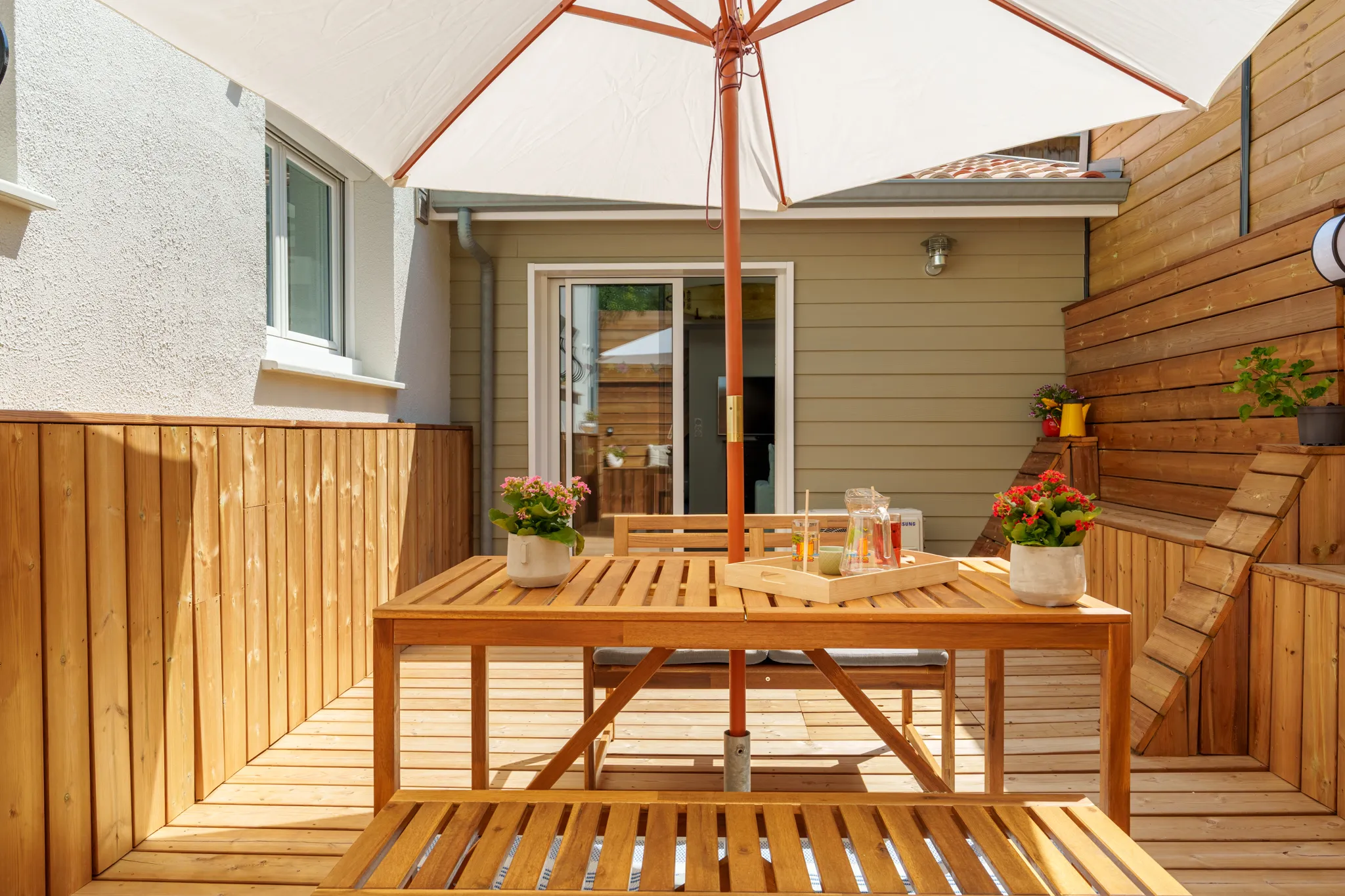 Terrasse ensoleillée et salon de jardin en bois.