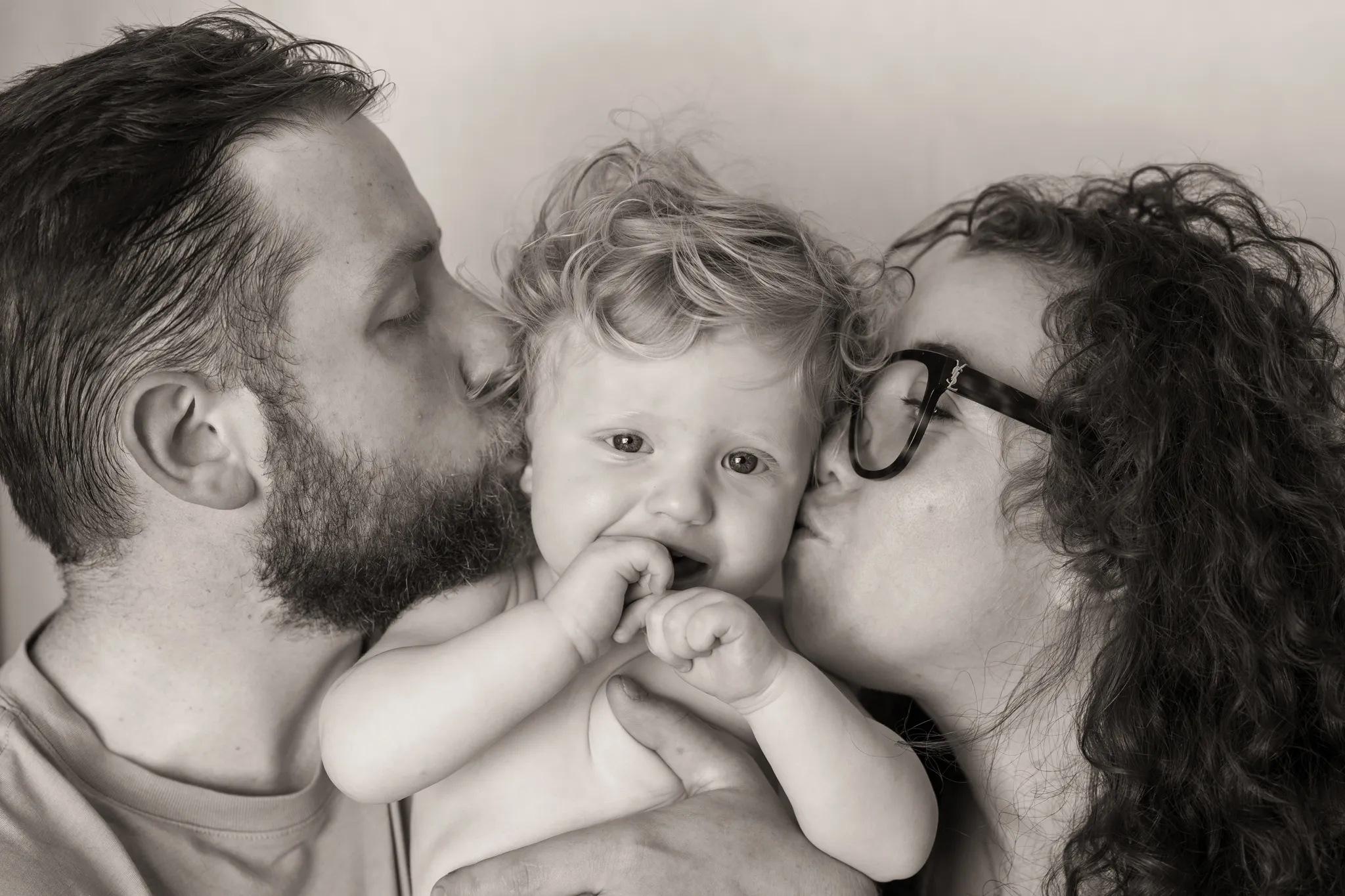 Visage bébé espiègle, embrassé par parents de chaque côté.