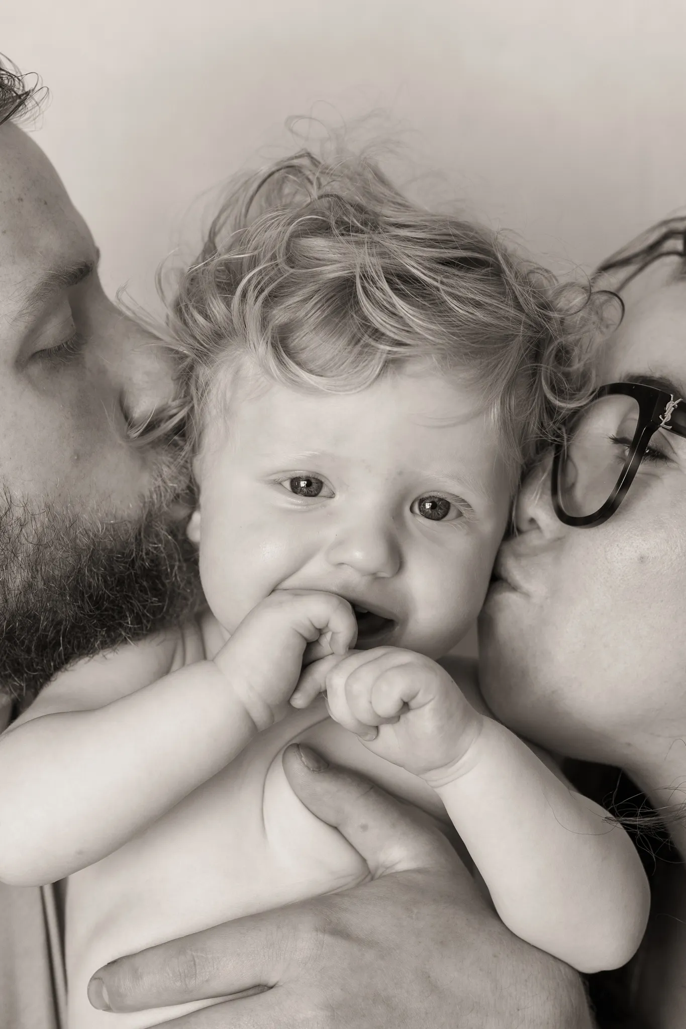 Bébé de face au regard brillant, parent de chaque coté l'embrassant.