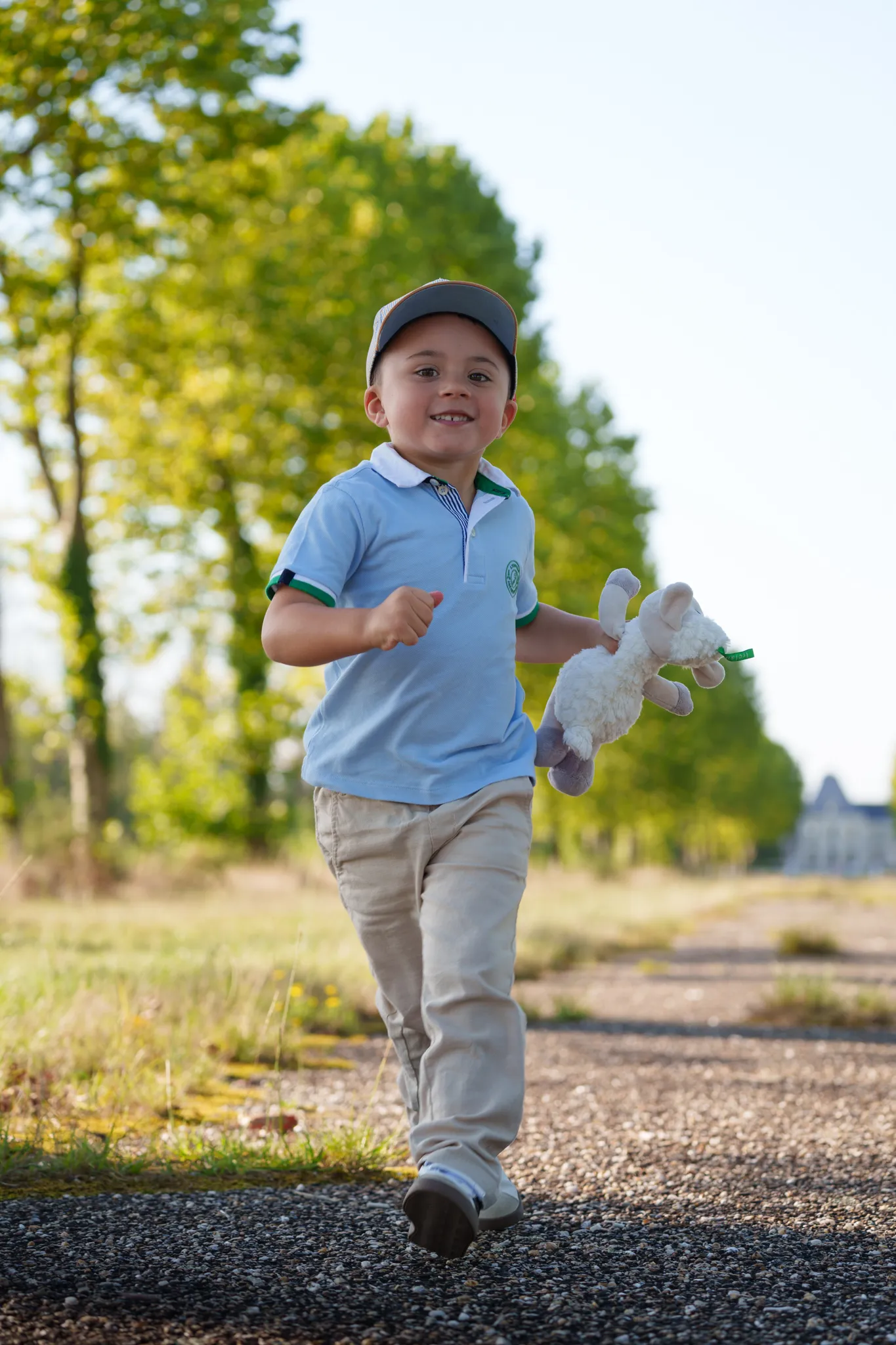 Jeune garçon rieur qui court sur un chemin ensoleillé, avec son doudou à la main.