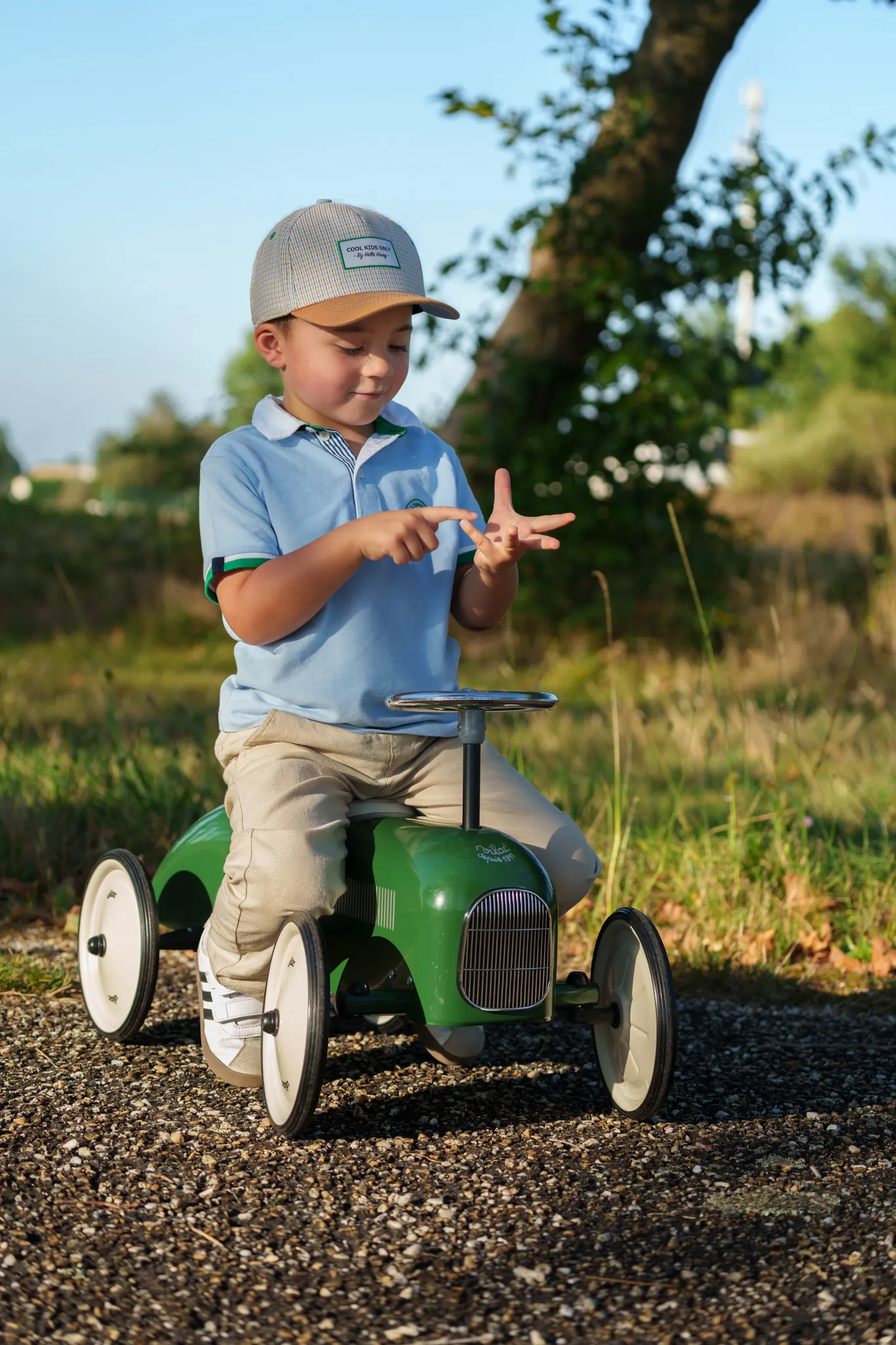 Petit garçon avec casquette, assis sur sa voiture à pédales, comptant sur ses doigts.