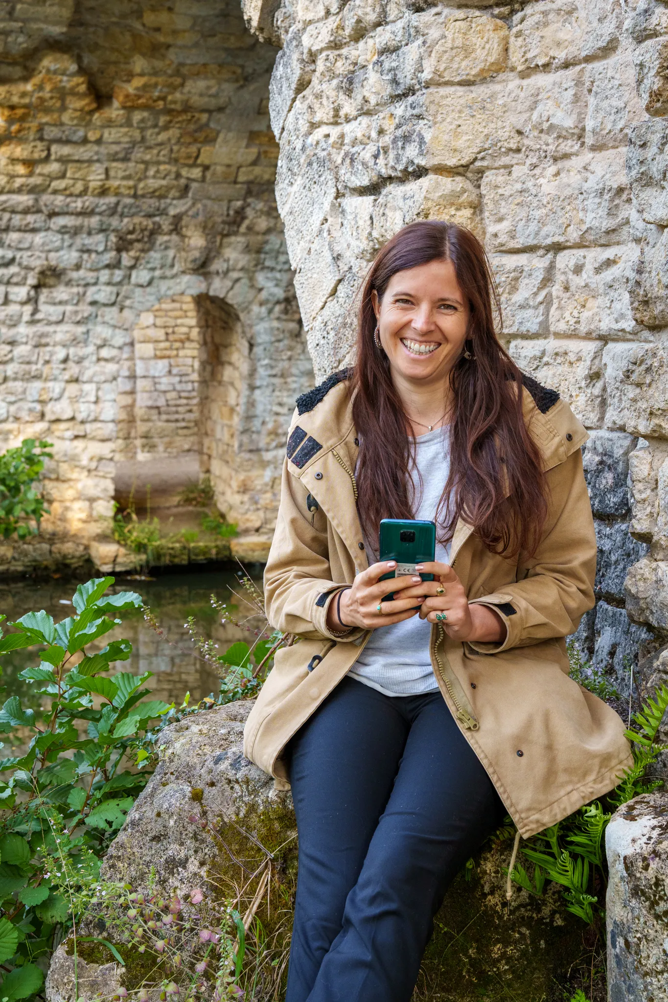 Femme radieuse avec téléphone,assise près pont de pierre.