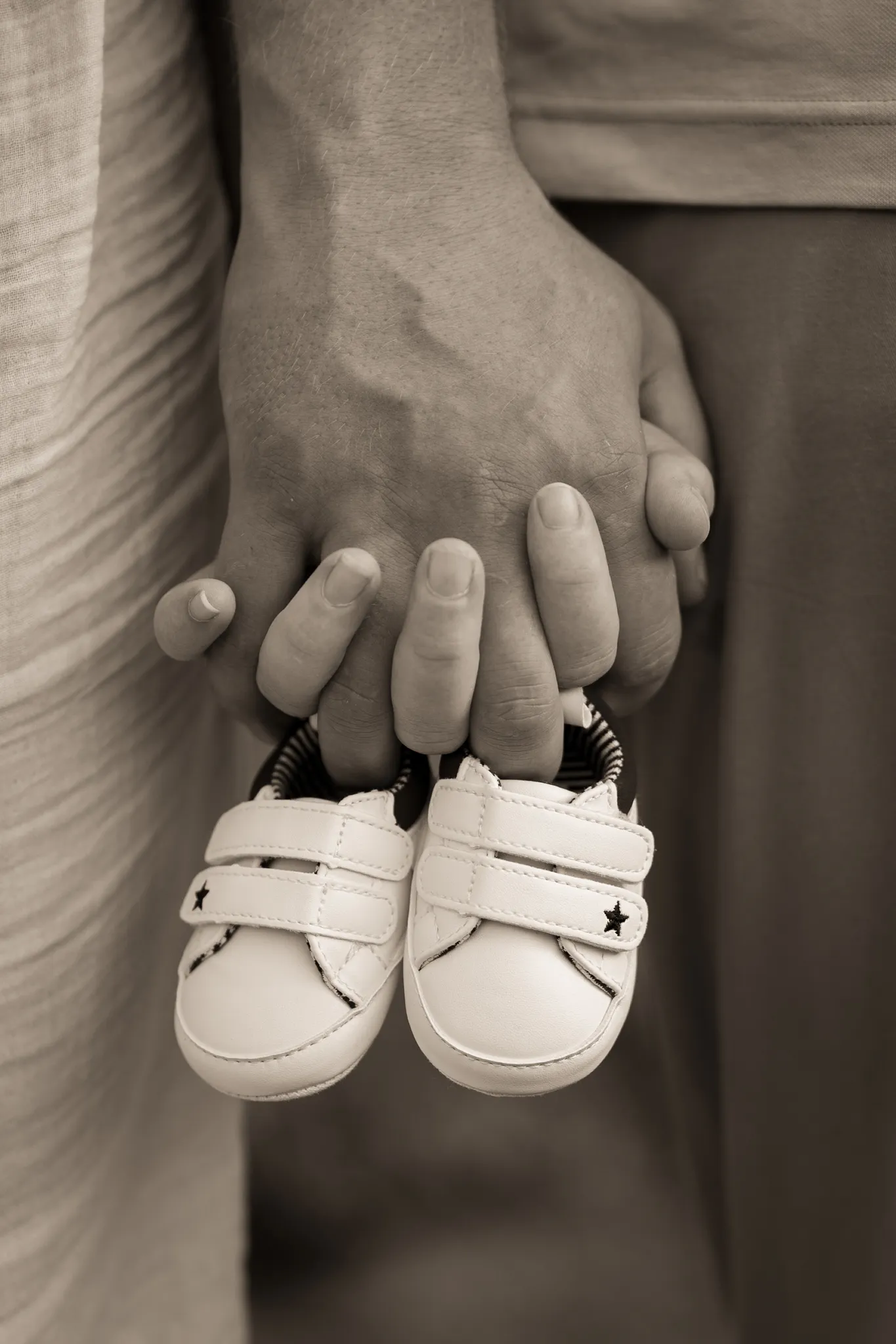 Deux mains de futurs parents, tenant des baskets de bébé.