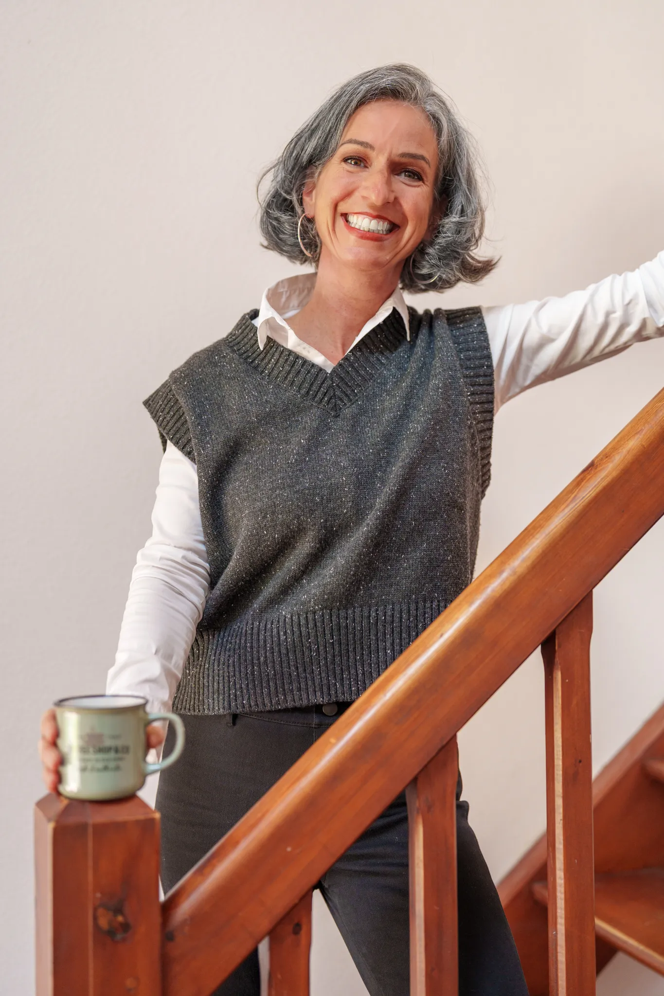 Femme joyeuse aux cheveux gris, sur escalier en bois.