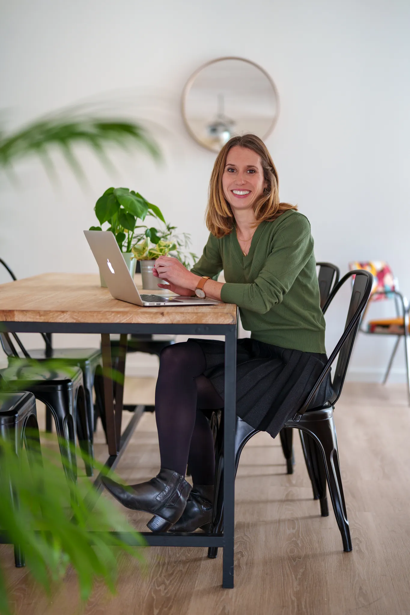 Entrepreneure souriante, attablée avec son ordinateur et entourée de plante.