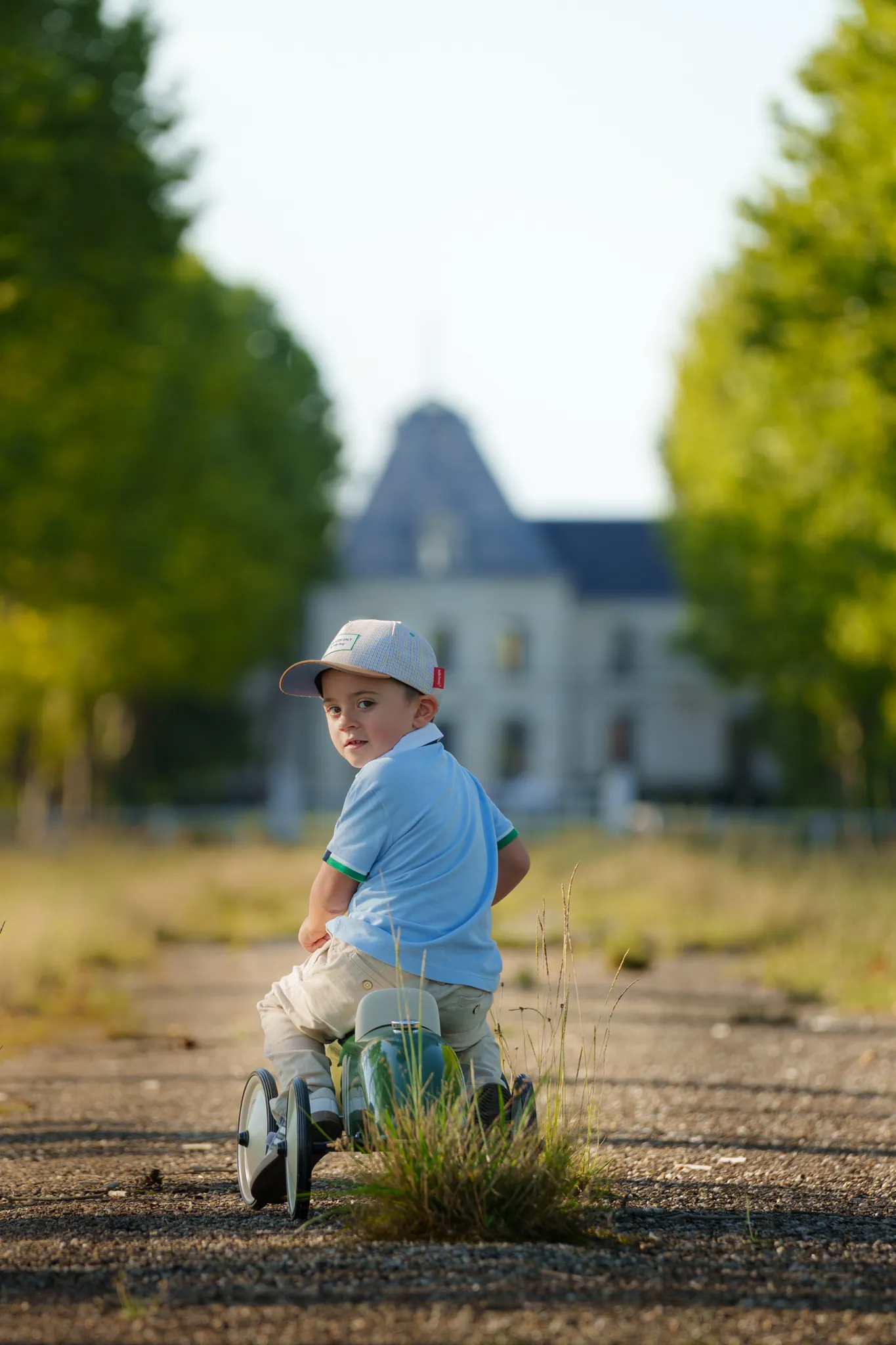 Jeune garçon sur sa voiturette, sur un chemin menant à un château.