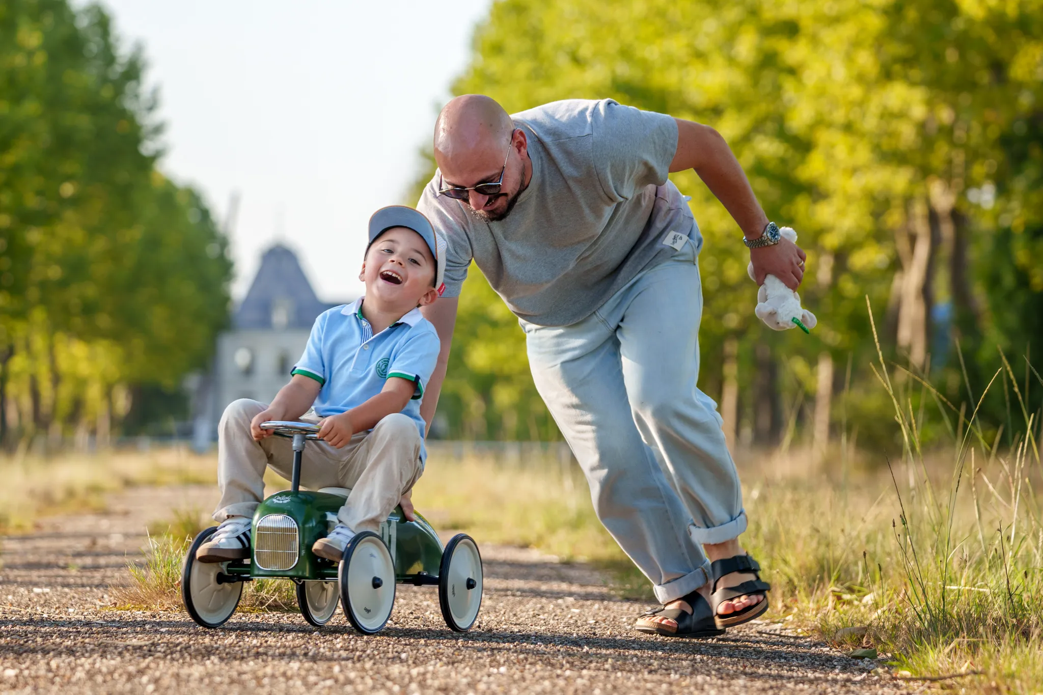 Père poussant son enfant rieur assis sur une voiture jouet.