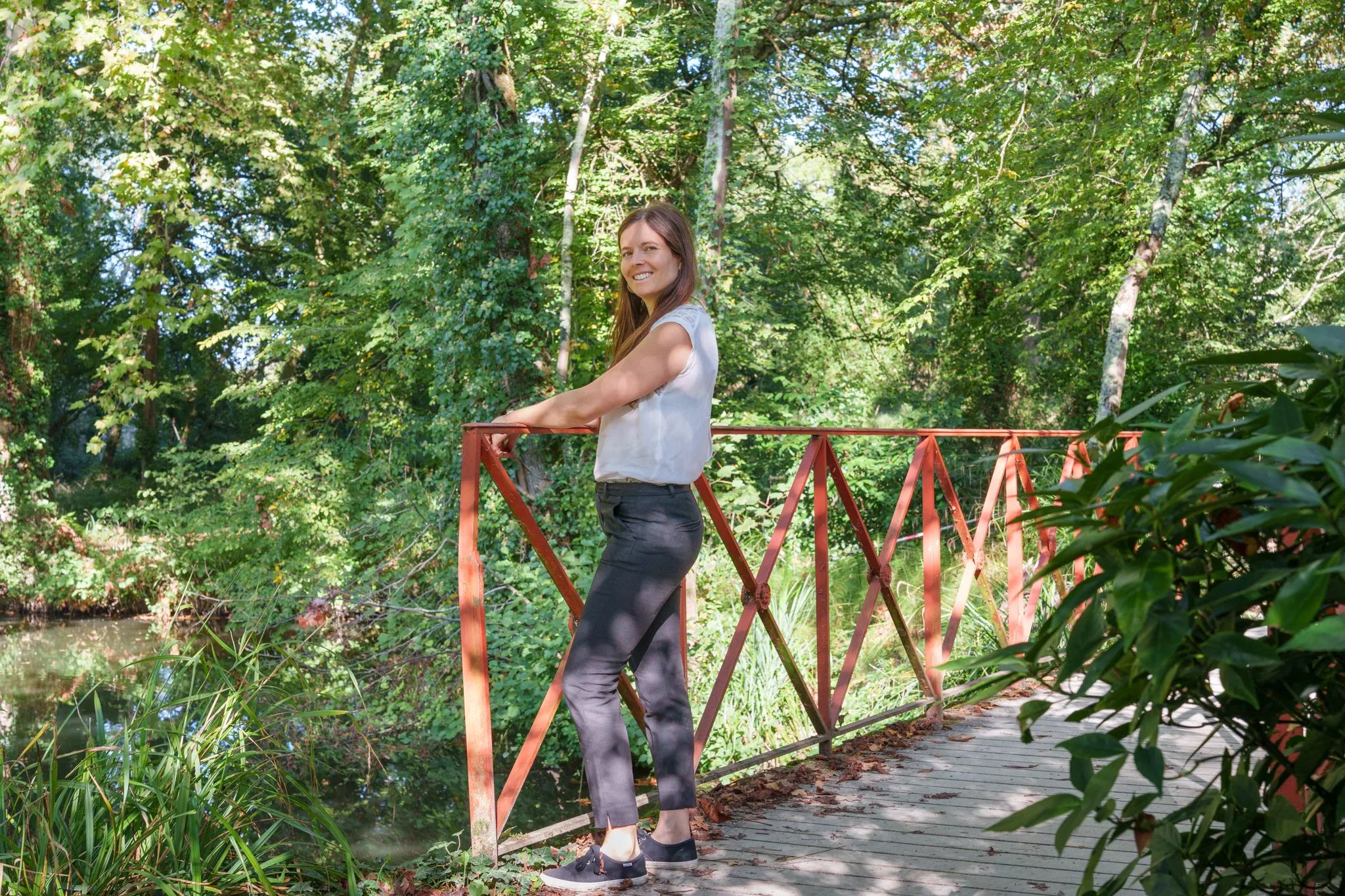Femme sur un pont aux barrières rouge, dans un parc verdoyant.