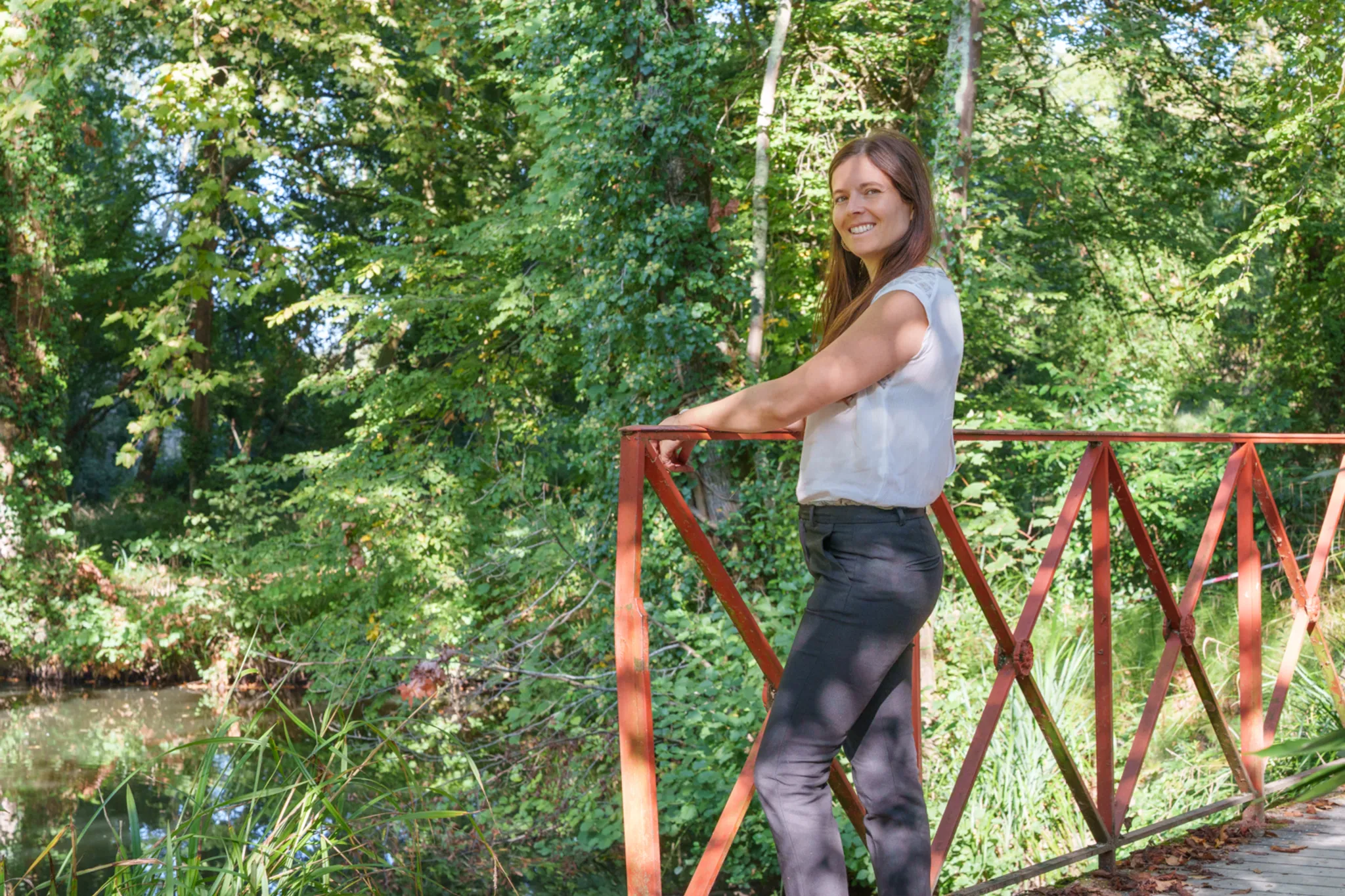 Femme sur un pont aux barrières rouge, dans un parc verdoyant.