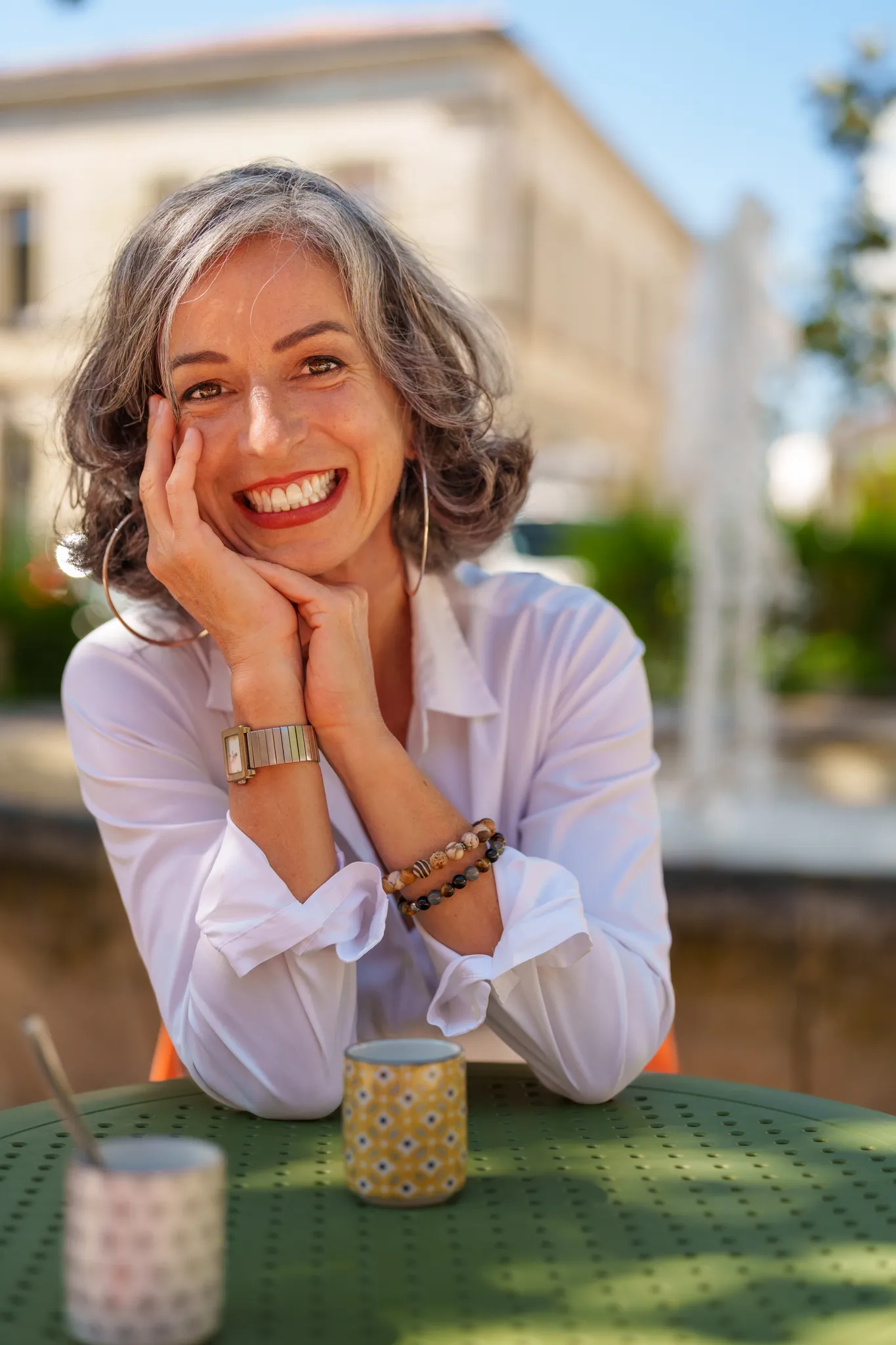 Coach souriante, accoudée à une table verte à l'extérieur