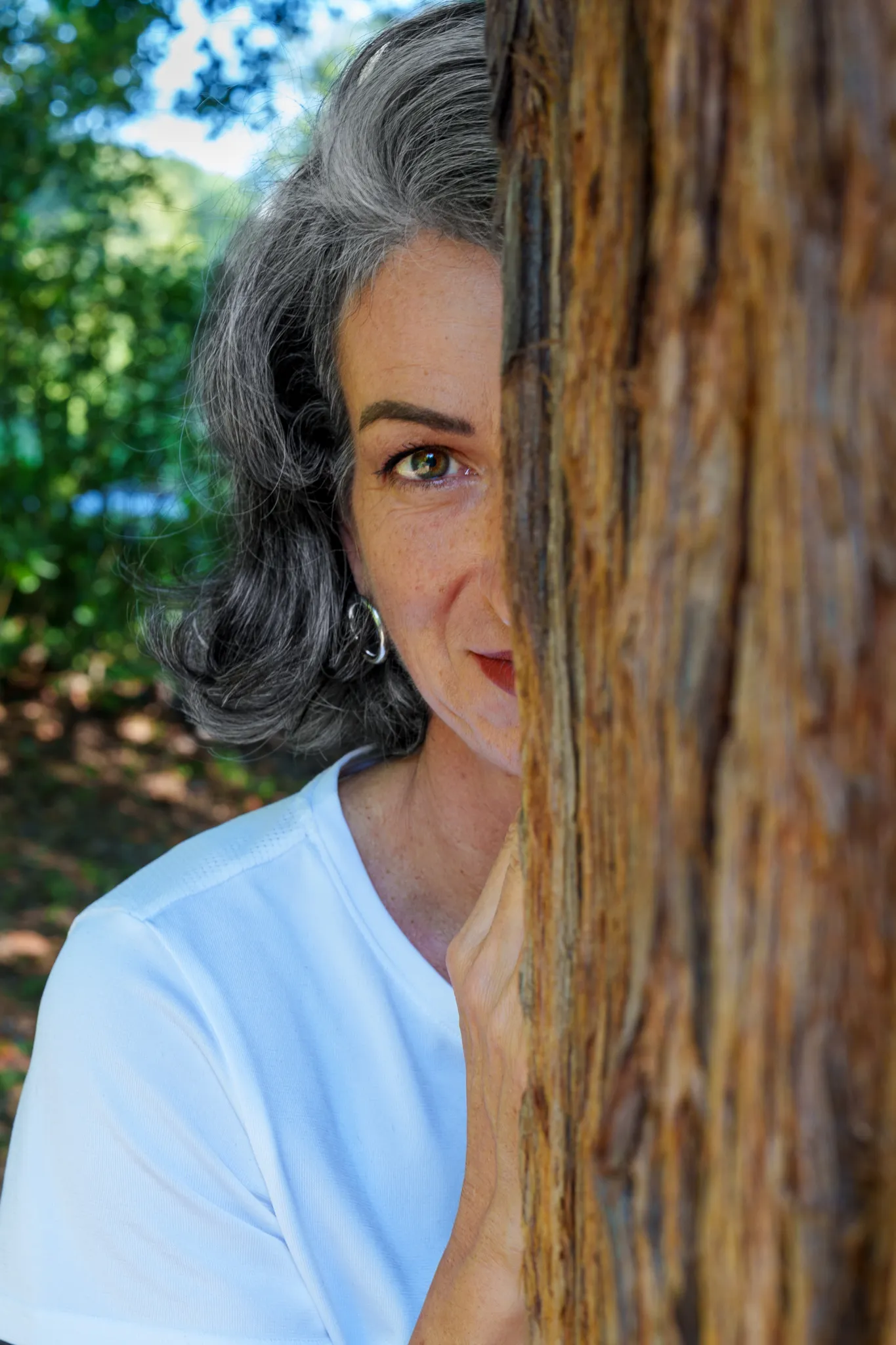 Discrète, la moitié du visage cachée par un tronc d'arbre.