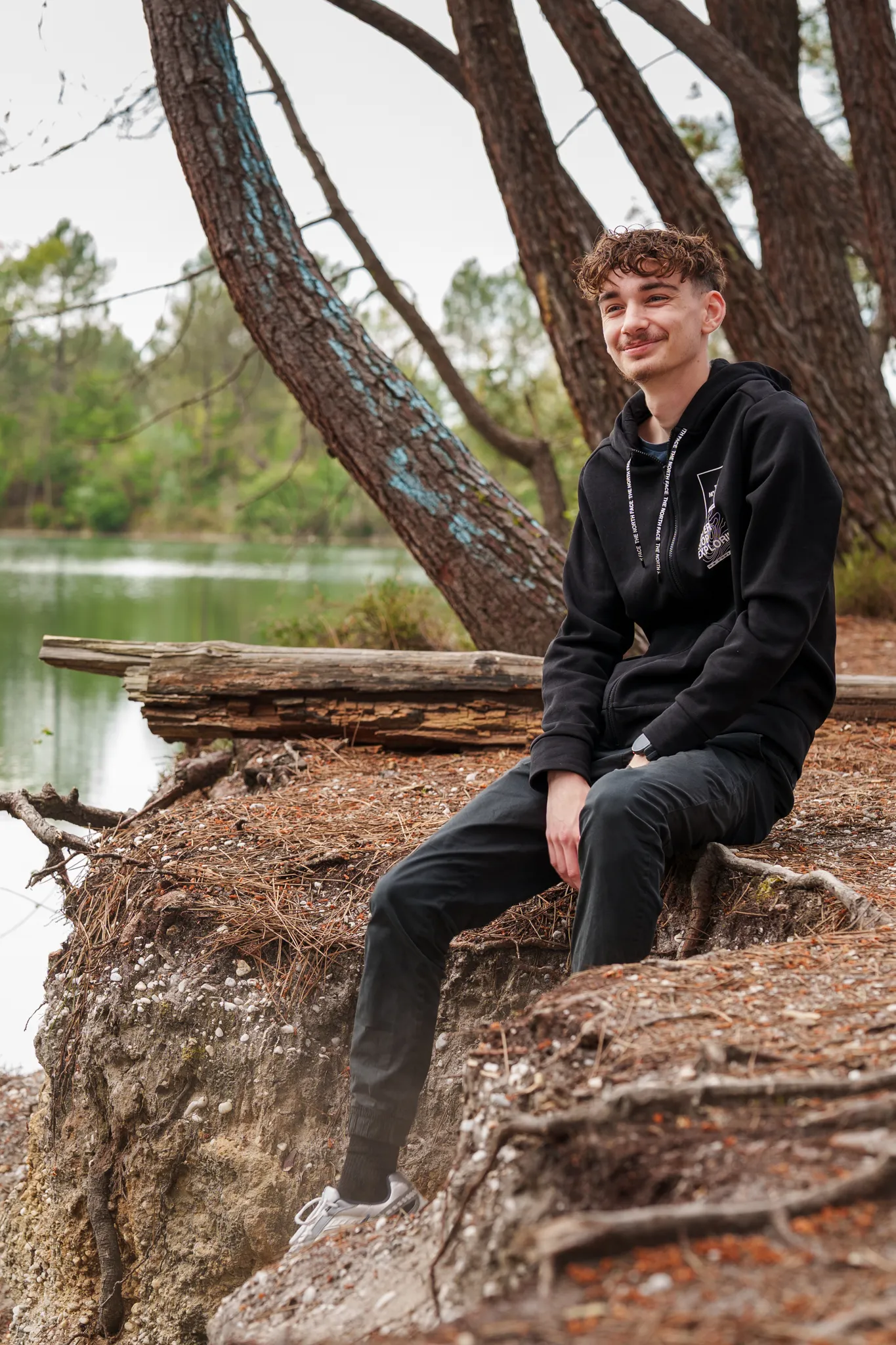 Jeune homme assis au bord d'un lac, en forêt.
